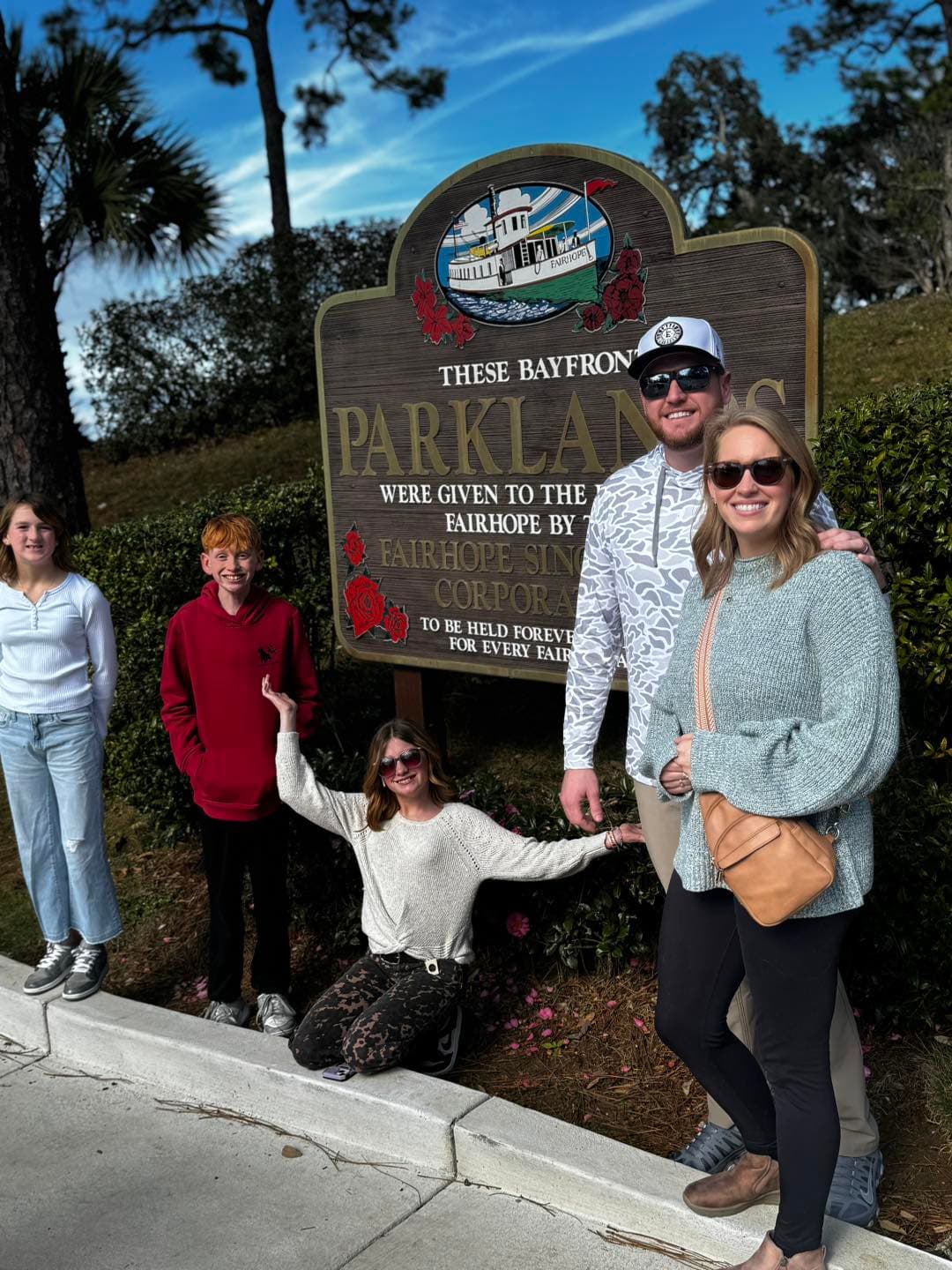 A smiling family of five poses in front of a large Fairhope Bayfront Parklands sign.